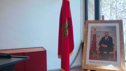 Drapeau du Maroc dressé sur sa hampe à côté du portrait encadré du roi Mohammed VI, dans une salle de réunion