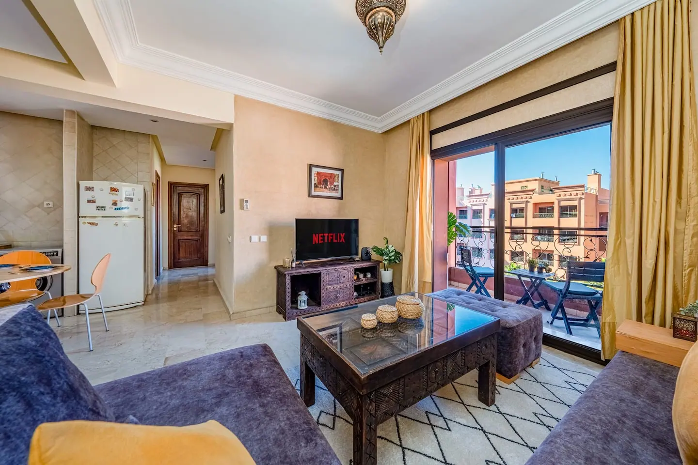 Salon d'un appartement à Marrakech avec table basse en bois sculpté, tapis berbère et baie vitrée ouverte sur un balcon
