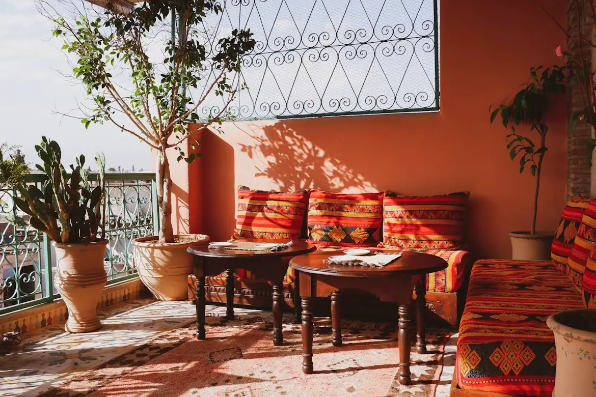Terrasse marocaine ocre avec banquettes couvertes de coussins berbères et tables rondes en bois sculpté