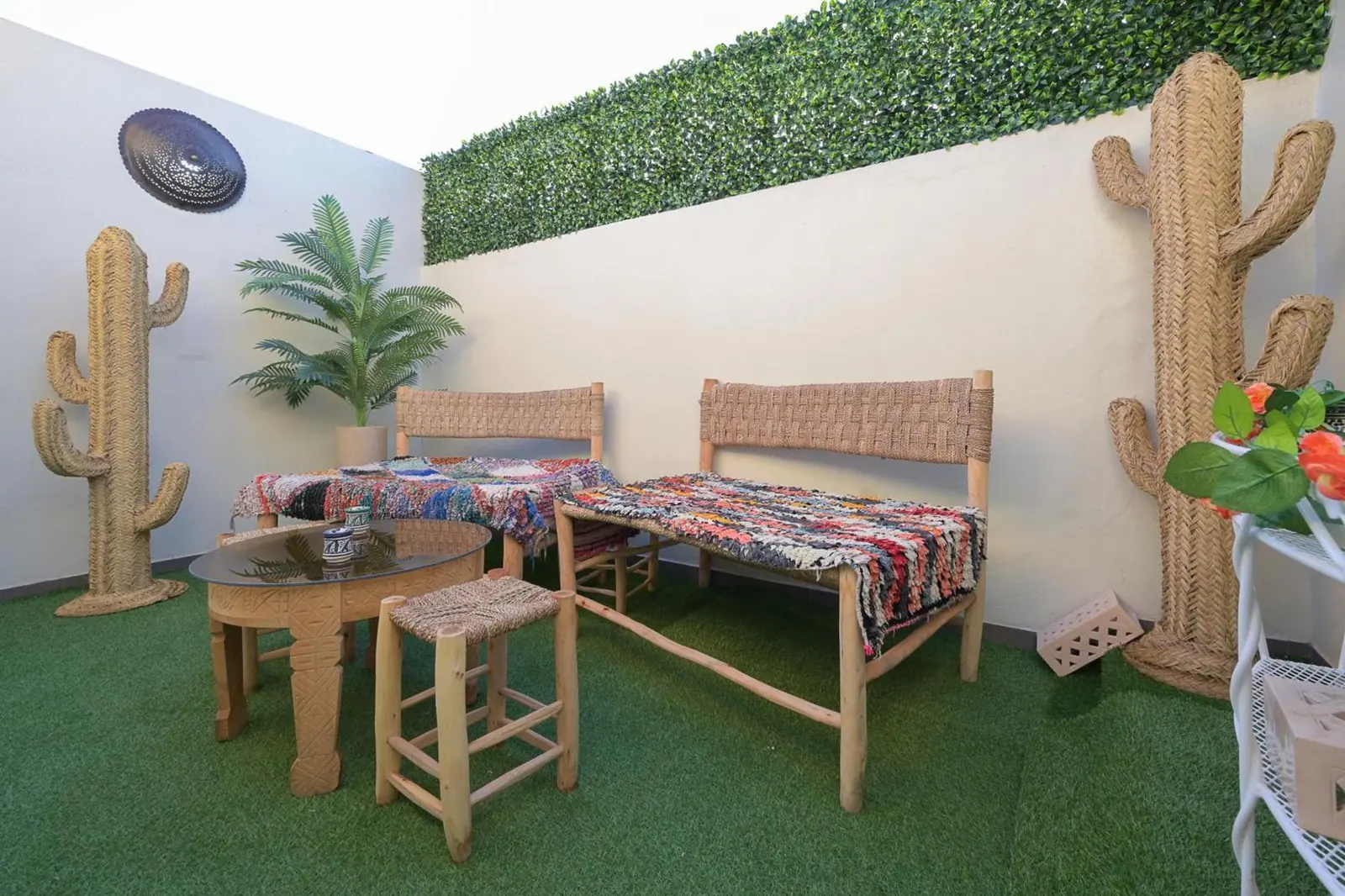 Terrasse marocaine aménagée avec banquettes en bois, tapis boucherouite colorés et cactus décoratifs en corde tressée, à Marrakech