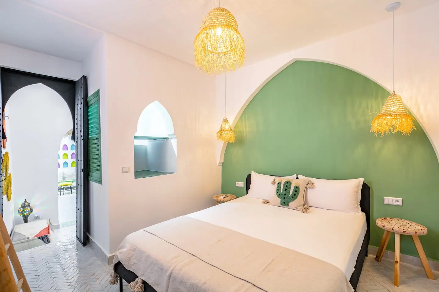Chambre d'un logement de la médina de Marrakech avec arche verte, suspensions en raphia et lit préparé