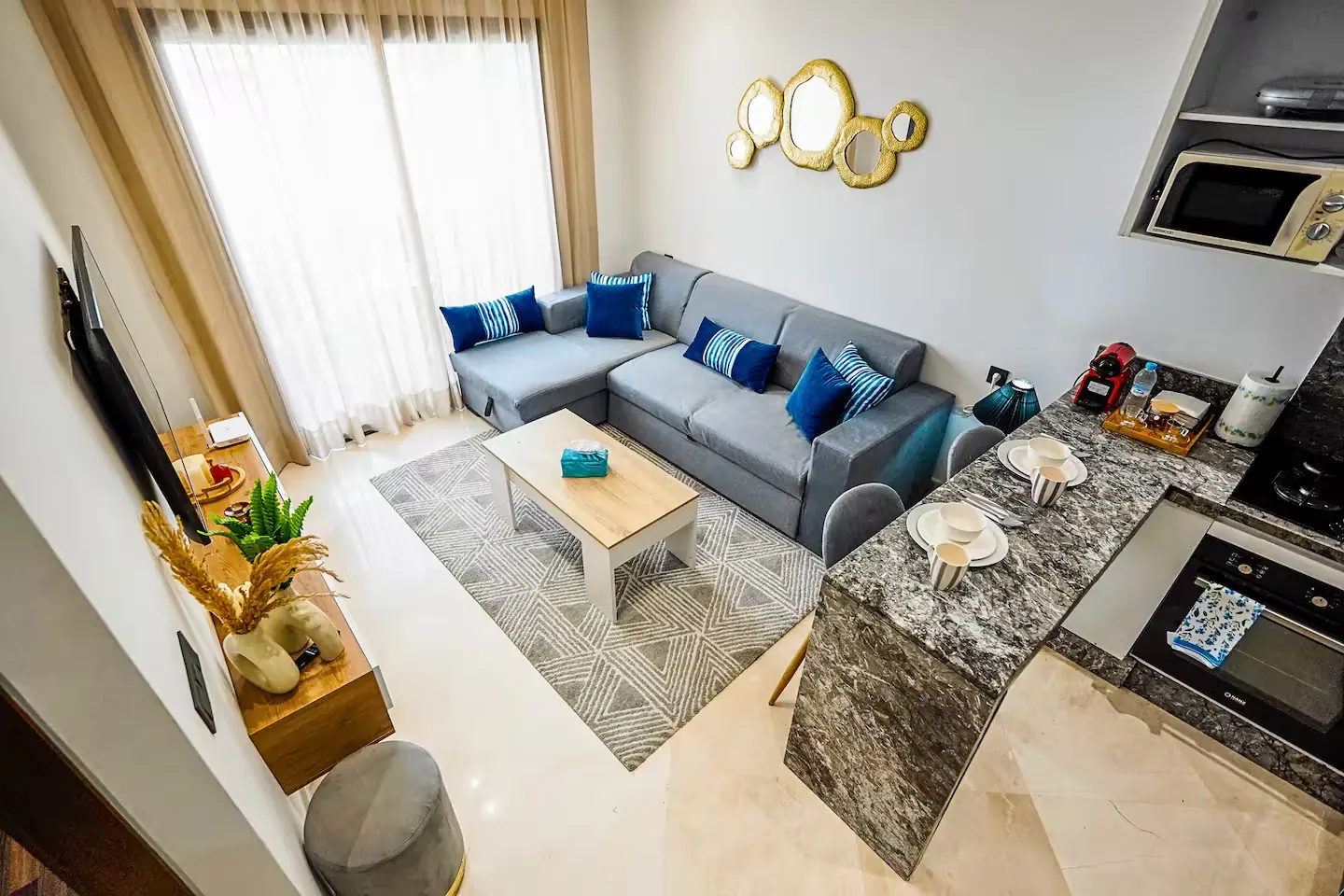 Séjour ouvert sur une cuisine dans un appartement de Casablanca, avec canapé d'angle gris et îlot en marbre dressé