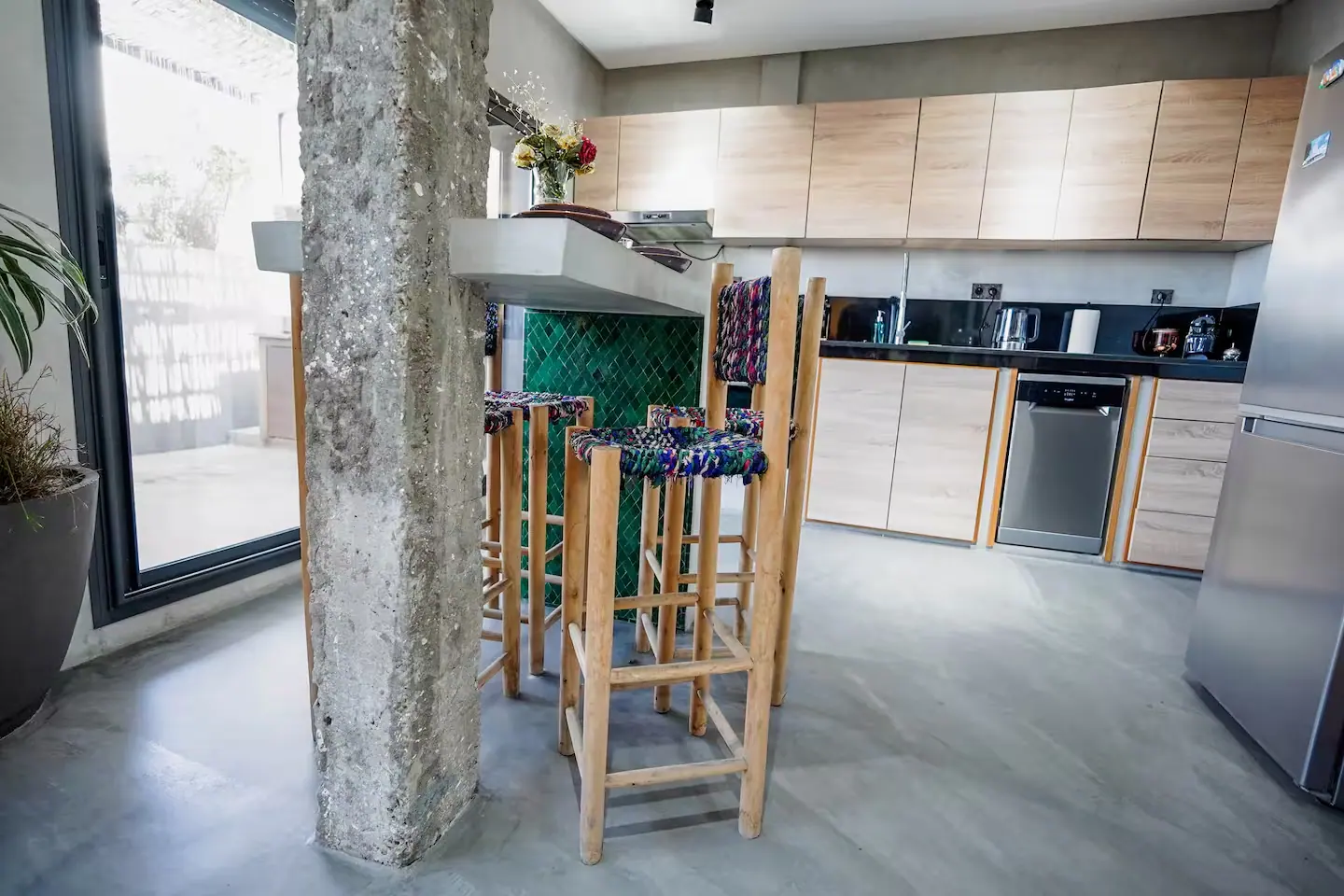 Cuisine ouverte d'un loft à Casablanca en béton ciré, avec tabourets en bois et crédence de zelliges verts