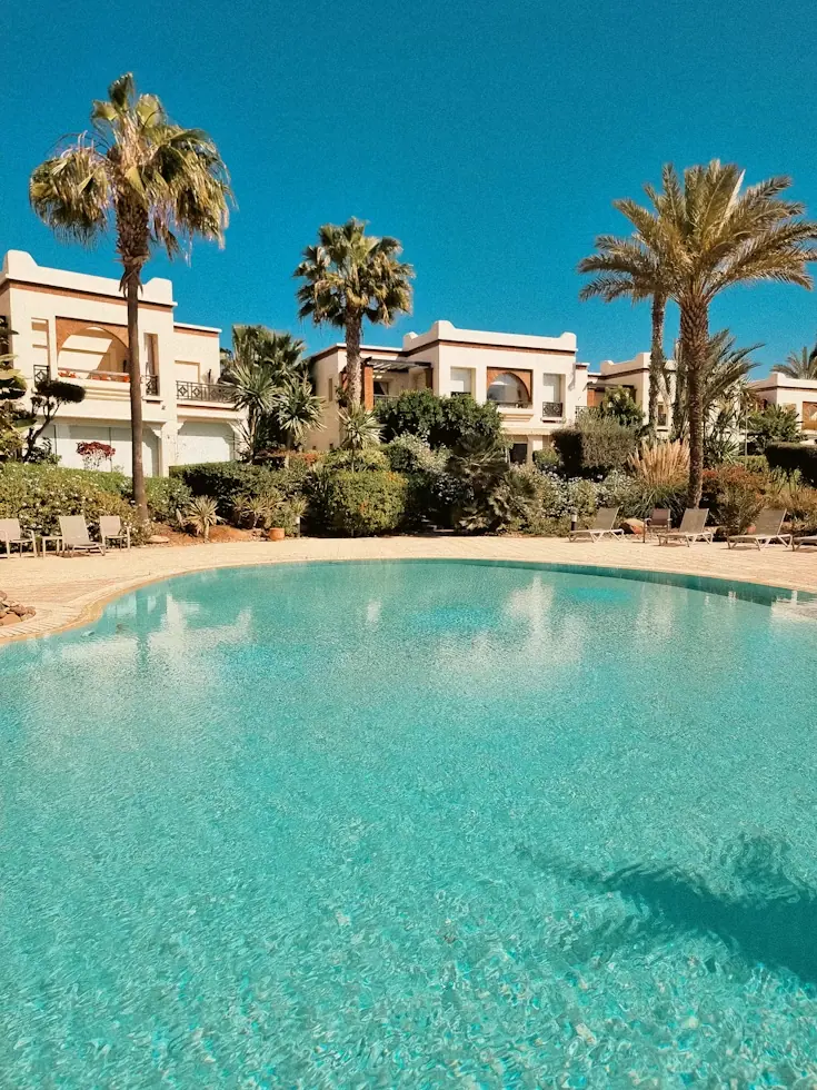 Grande piscine bordée de palmiers devant une résidence blanche de style marocain à Agadir, sous un ciel bleu
